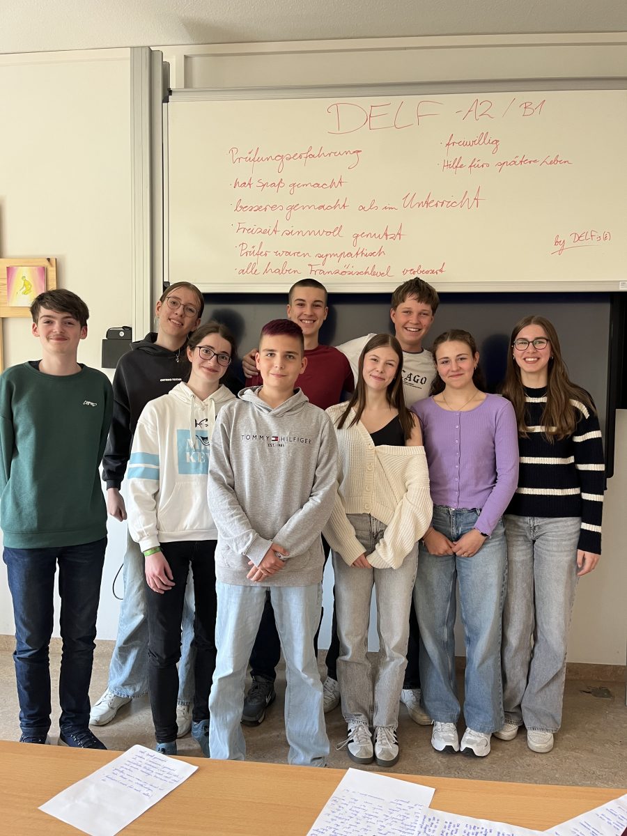 Man sieht eine Gruppe aus Schülerinnen und Schülern, die alle lachen, vor einer Tafel